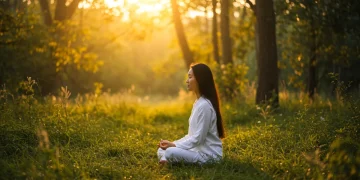 Woman meditating in lush forest at sunrise, embodying spiritual wellness through nature connection.